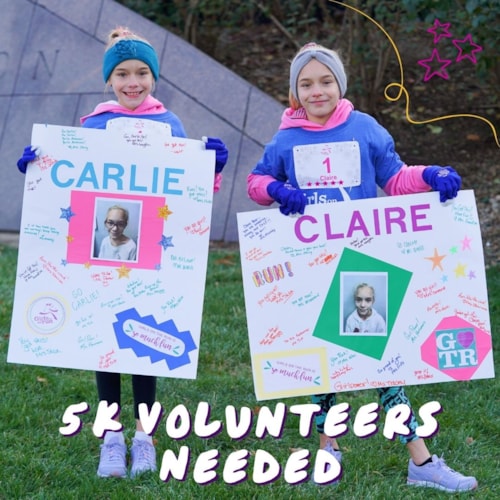 Two girls bundled up for fall weather holding cheers signs on a grassy lawn in a park. Text says 'Volunteers Needed.'